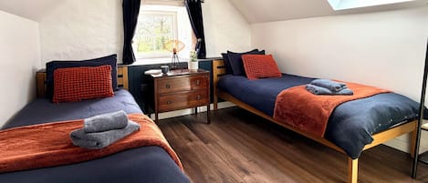 A room with two beds, a wooden dresser, a window with curtains, and a skylight.