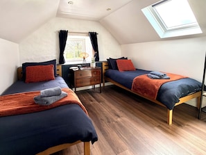 Una habitación con dos camas, un aparador de madera, una ventana con cortinas y un tragaluz.
