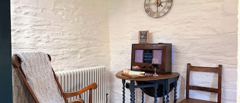 A room with a rustic aesthetic, featuring a wooden chair, a small table with a television, and a wall clock.