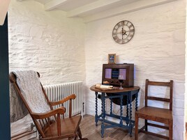 A room with a rustic aesthetic, featuring a wooden chair, a small table with a television, and a wall clock.