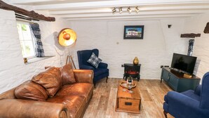 A cozy living room with a brown leather sofa, a blue armchair, a wooden coffee table, a television, and a wood-burning stove. - Pensarngerrig (Llandysul)