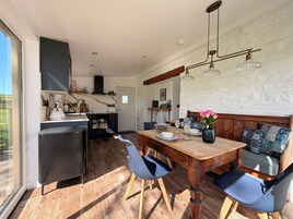 A modern kitchen with a dining area, wooden furniture, and a view through a large window.
