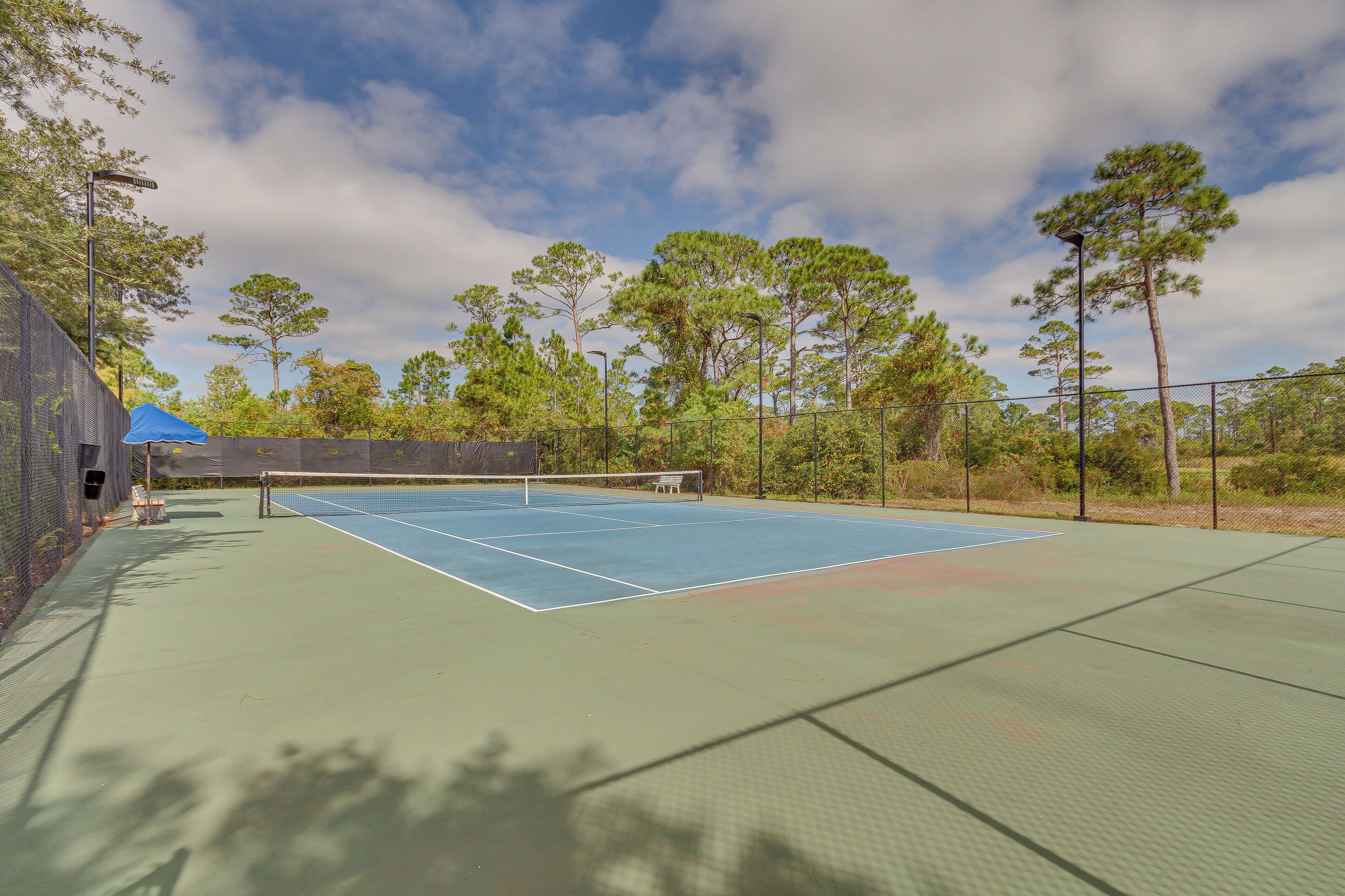 An outdoor tennis court with a net, surrounded by trees and a fence.