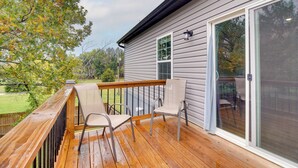 Une terrasse en bois avec deux chaises et une porte vitrée donnant sur un patio abrité.