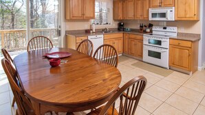 Een moderne keuken met houten kastjes, een eettafel met stoelen en een groot raam met uitzicht op bomen.