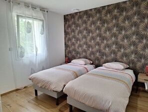 Makuuhuoneessa on kaksi sänkyä, ikkunassa läpikuultavat verhot ja kuviollinen sängynpääty.