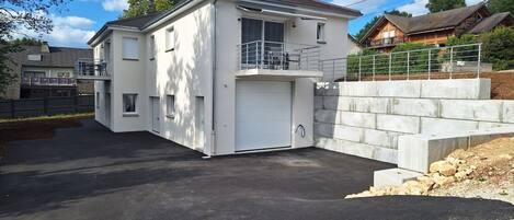 Una casa de dos pisos con garaje, un balcón y un muro de contención de piedra.