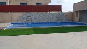Una piscina amb mur de pedra i gespa artificial.