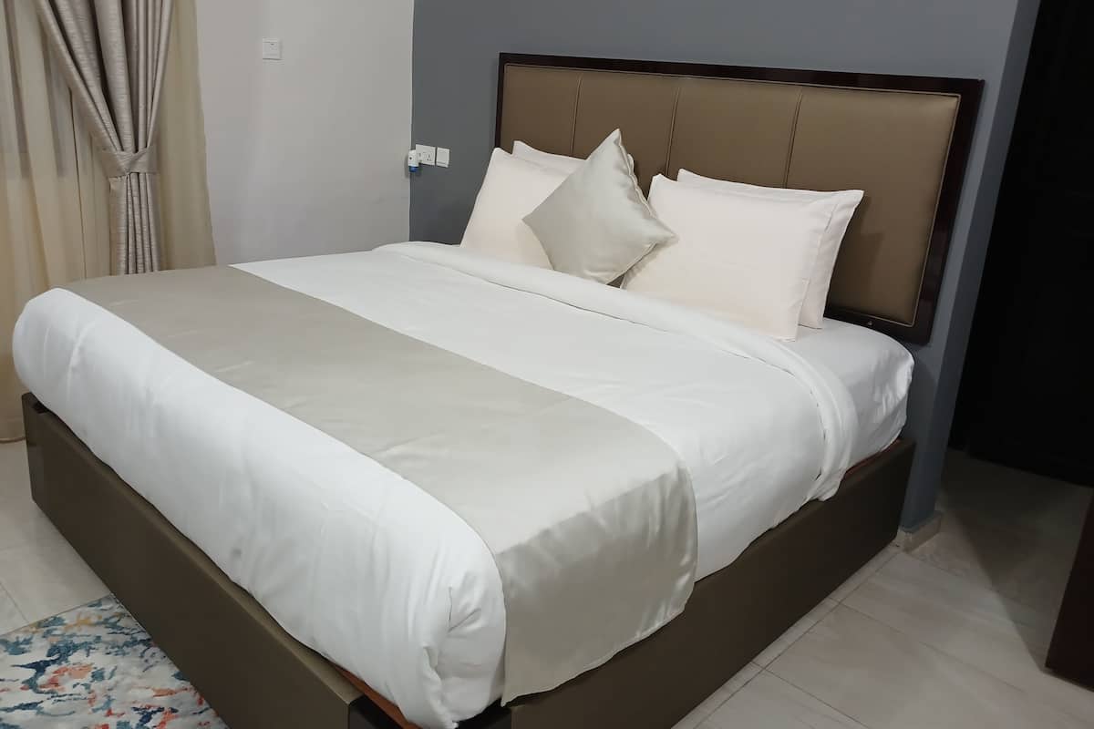 Un lit bien fait, avec une tête de lit beige et du linge de lit blanc, dans une chambre d’hôtel.