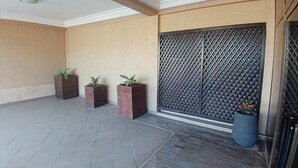 Zona exterior coberta amb paviment de rajoles, tres planters quadrats amb plantes, una gran porta metàl·lica i una planta en test amb prop de la porta.
