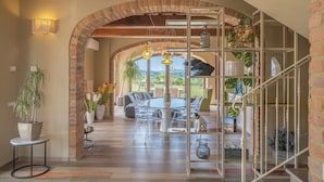 An open-plan living area with a dining table, chairs, and a sofa. There is a staircase with a railing and a view of the outdoors. - Villa Tosca (Peccioli)
