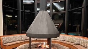 A circular stone fire pit with a conical roof in a lobby area with large windows and a high ceiling. - Spectacular Ocean View - Heated 80° Pool - Seascape (Aptos)