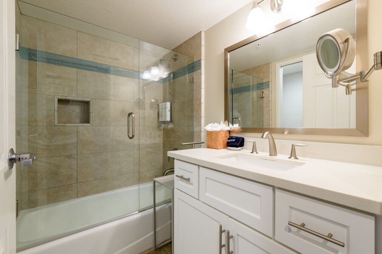 A modern bathroom with a glass-enclosed shower, a large mirror, and a vanity with a sink and storage drawers.