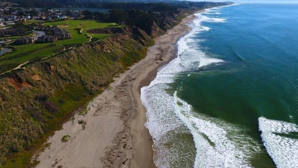 An aerial view of a coastal area with a sandy beach, a clear blue ocean, and a residential area with houses and greenery. - Spectacular Ocean View - Heated 80° Pool - Seascape (Aptos)