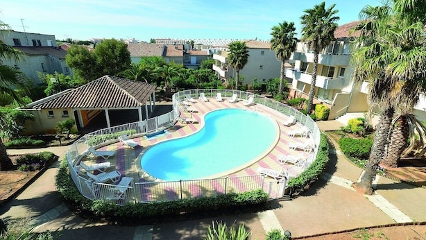 A swimming pool with a curved design, surrounded by lounge chairs and a fence. - Le Mayflower - One Bedroom Apartment, Sleeps 4 (Le Grau-du-Roi)