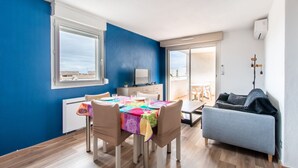 A modern living room with a dining area, featuring a blue wall, wooden flooring, and a grey sofa. - Le Mayflower - One Bedroom Apartment, Sleeps 4 (Le Grau-du-Roi)