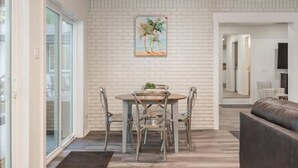 A dining area with a white brick wall, a painting of palm trees, and a round table with chairs. - Luxury Lakefront Escape, Beach Volleyball, Kayaks, Fire Pit Hot Tub & Game Room! (Hot Springs)