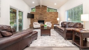 A modern living room with a stone fireplace, leather sofas, and a flat-screen TV. - Luxury Lakefront Escape, Beach Volleyball, Kayaks, Fire Pit Hot Tub & Game Room! (Hot Springs)