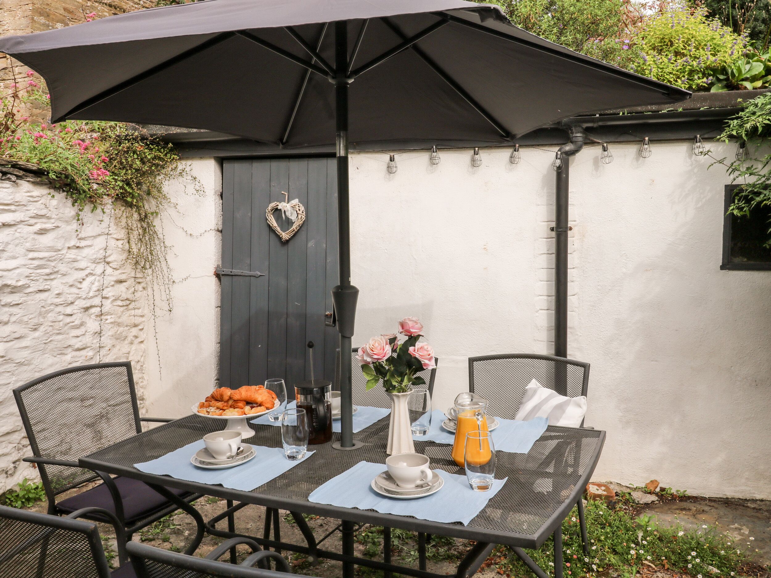Un patio al aire libre con una mesa preparada para el desayuno, con croissants, café y jugo.