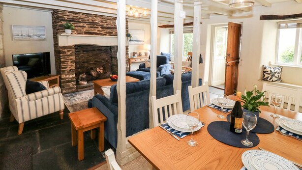 A cozy living room with a fireplace, a dining area with a wooden table set for two, and a comfortable seating area with sofas. - Alexander's Cottage (Kingsbridge)