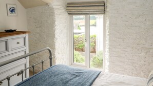 A bedroom with a bed, a dresser, a window with a view of greenery, and a white textured wall. - Alexander's Cottage (Kingsbridge)