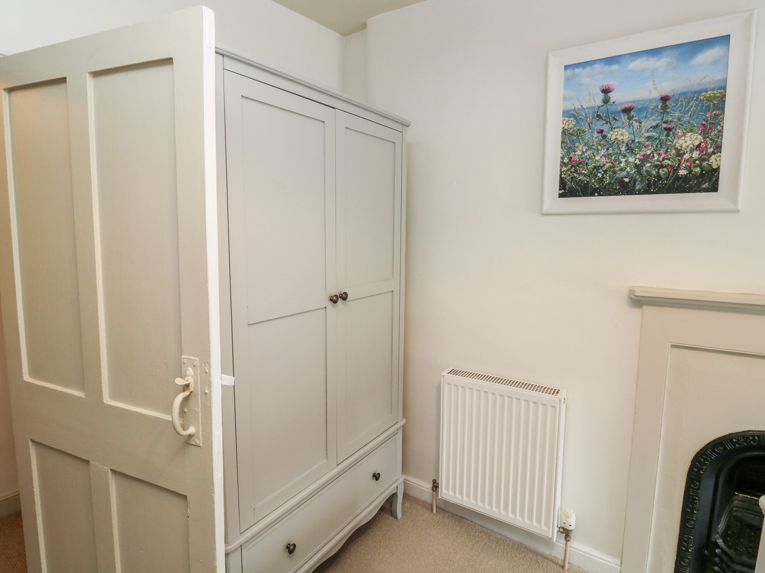 Une pièce avec une armoire blanche, un radiateur et un tableau encadré accroché au mur.