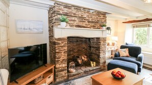A cozy living room with a stone fireplace, a television, a comfortable sofa, and a small table with fruit. - Alexander's Cottage (Kingsbridge)