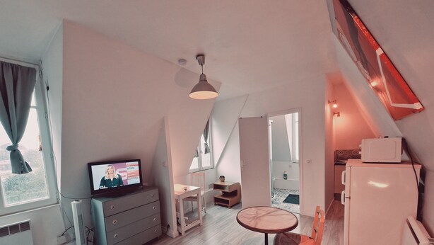 A compact, modern room with a television, a small dining table, and a refrigerator. - Location Saisonnière, Meublée, Appartement Type Studio à Sèvres (Sèvres)