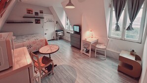 A cozy, well-lit attic bedroom with a bed, desk, chair, and a TV. - Location Saisonnière, Meublée, Appartement Type Studio à Sèvres (Sèvres)
