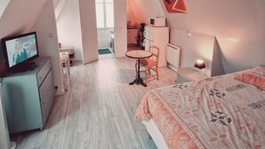 A bedroom with a bed, a desk, and a television. There is a kitchen area in the background. - Location Saisonnière, Meublée, Appartement Type Studio à Sèvres (Sèvres)