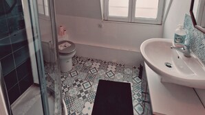 A bathroom with a shower, toilet, and sink. There is a window providing natural light. - Location Saisonnière, Meublée, Appartement Type Studio à Sèvres (Sèvres)