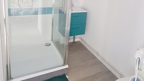 Une salle de bain moderne avec une douche à parois de verre, des toilettes blanches et un meuble de couleur turquoise.