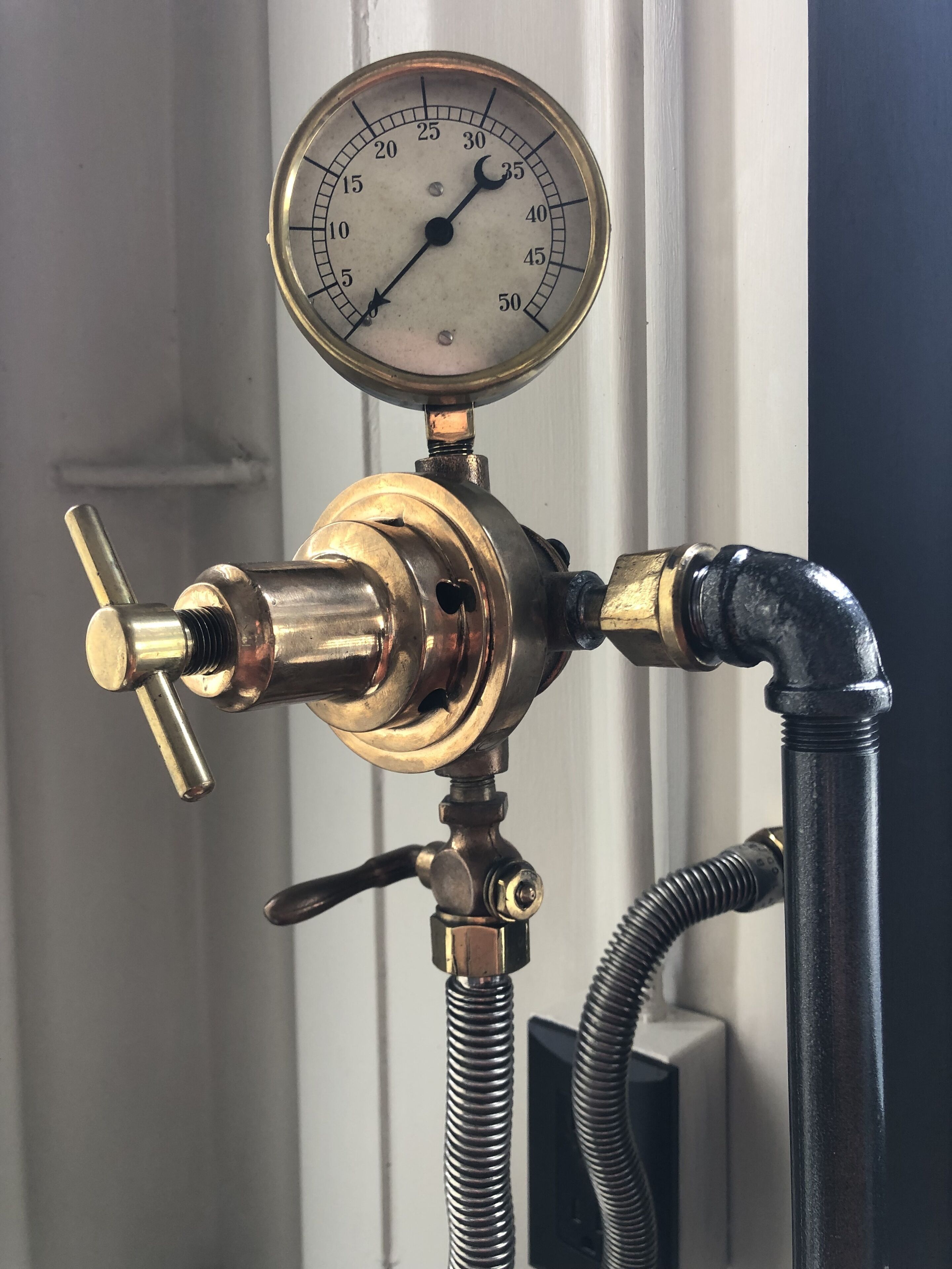 A brass water meter with a gauge, a valve, and a flexible hose.