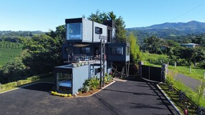 Un edificio moderno a più piani con facciata in vetro, area salotto esterna e vista sulle colline circostanti.