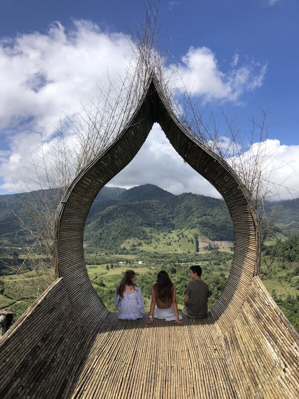 Un groupe de personnes est assis sur une structure en bambou, d’où l’on peut admirer un paysage montagneux.