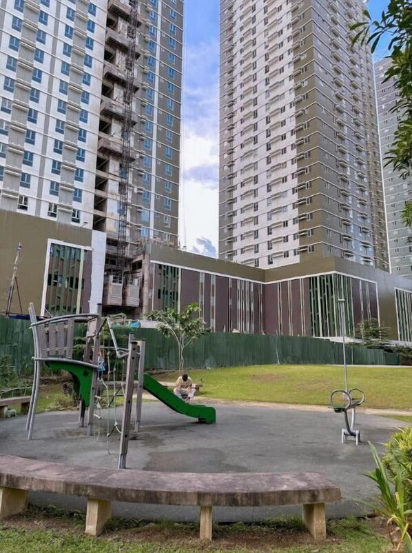 Residents can enjoy a playground with a slide and swing set in a paved area surrounded by benches.