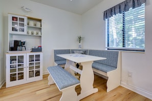 A compact living space with a white cabinet, a bench, a small table, and a window with blinds.