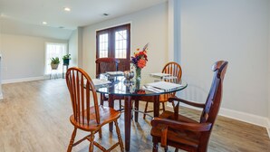 Un coin repas avec une table en verre entourée de chaises en bois, un vase rempli de fleurs et une fenêtre avec des rideaux.