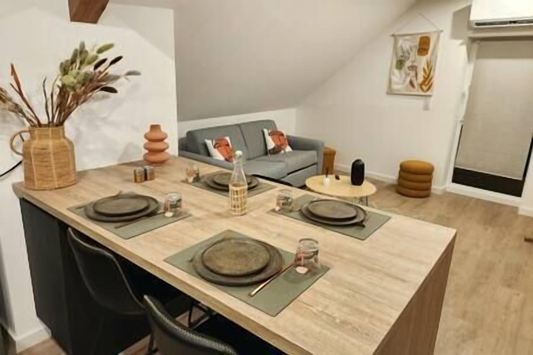 A dining area with a long table set for four, a sofa, and a small round table in a modern apartment.