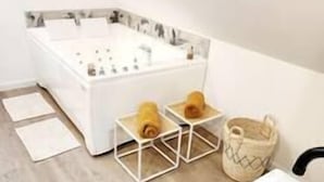 Ein modernes Badezimmer mit einer weißen Badewanne, einem Waschbecken und zwei geometrischen Nachttischen mit Handtüchern.