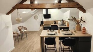Eine moderne Küche mit Holzbalkendecke, einem Essbereich mit zwei schwarzen Stühlen und einer kleinen Kochinsel mit einer Vase.