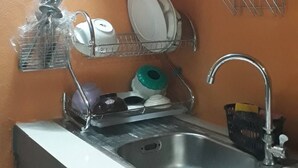 Een kleine keuken met een spoelbak, een afdruiprek en een bestekhouder.