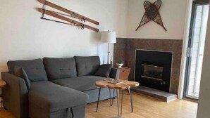 A modern living room with a grey sectional sofa, a small round table, and a fireplace. - Eagle River Retreat (Avon)