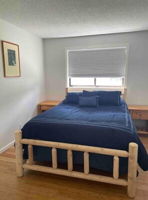 A bedroom with a wooden bed frame, a dark blue bedspread, and a window with blinds. - Eagle River Retreat (Avon)