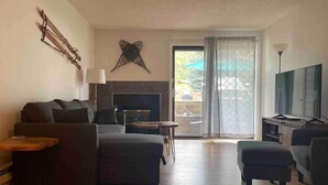 A modern living room with a sofa, a coffee table, a TV, and a fireplace. - Eagle River Retreat (Avon)