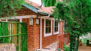 A brick building with a tiled patio, a green gate, and a potted plant. - Lushoto Views Cottage (Lushoto)