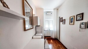 A narrow hallway with a white table and chair, a mirror, and a small kitchenette area with a window. - Casa Flora (Taranto)