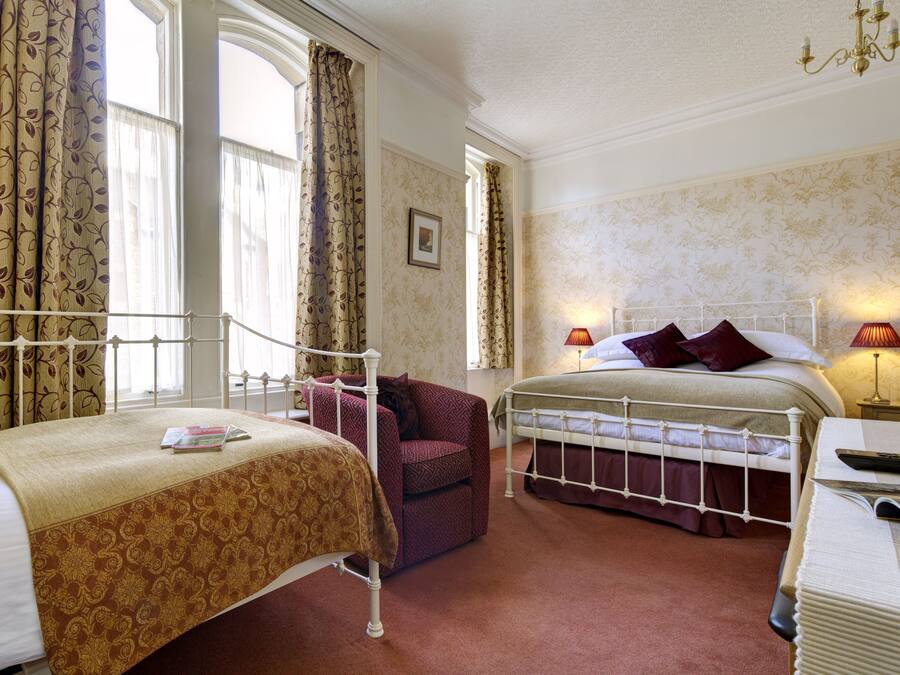 Una habitación de hotel con dos camas, un sillón rojo, una mesita de noche con lámparas y un espejo grande.