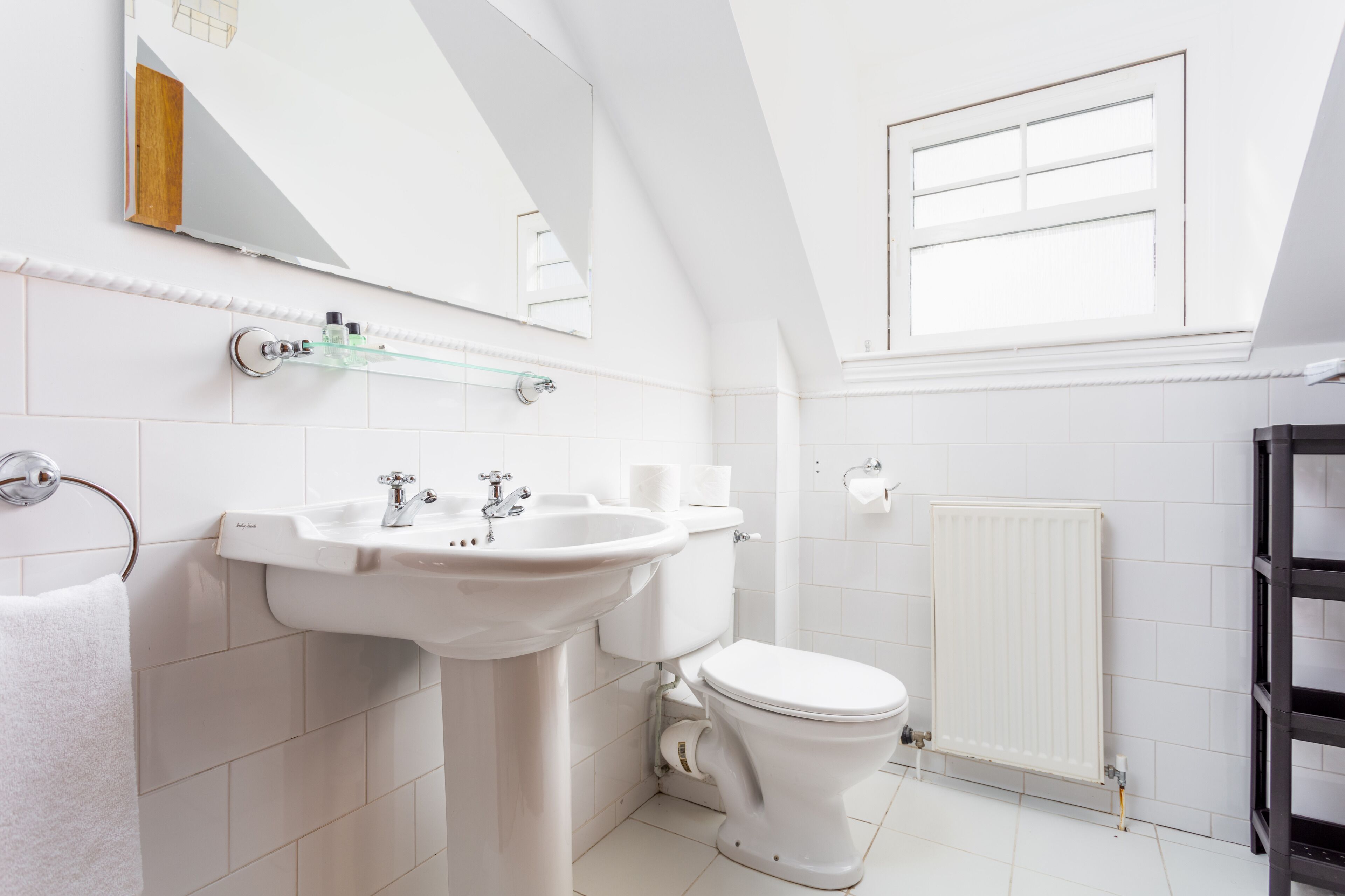 Une salle de bain moderne avec un lavabo, des toilettes et un radiateur, le tout de couleur blanche.