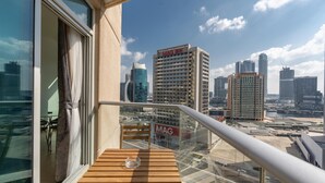 Un balcon doté d’une balustrade en verre, offrant une vue sur le paysage urbain, avec des immeubles de grande hauteur et un ciel dégagé.